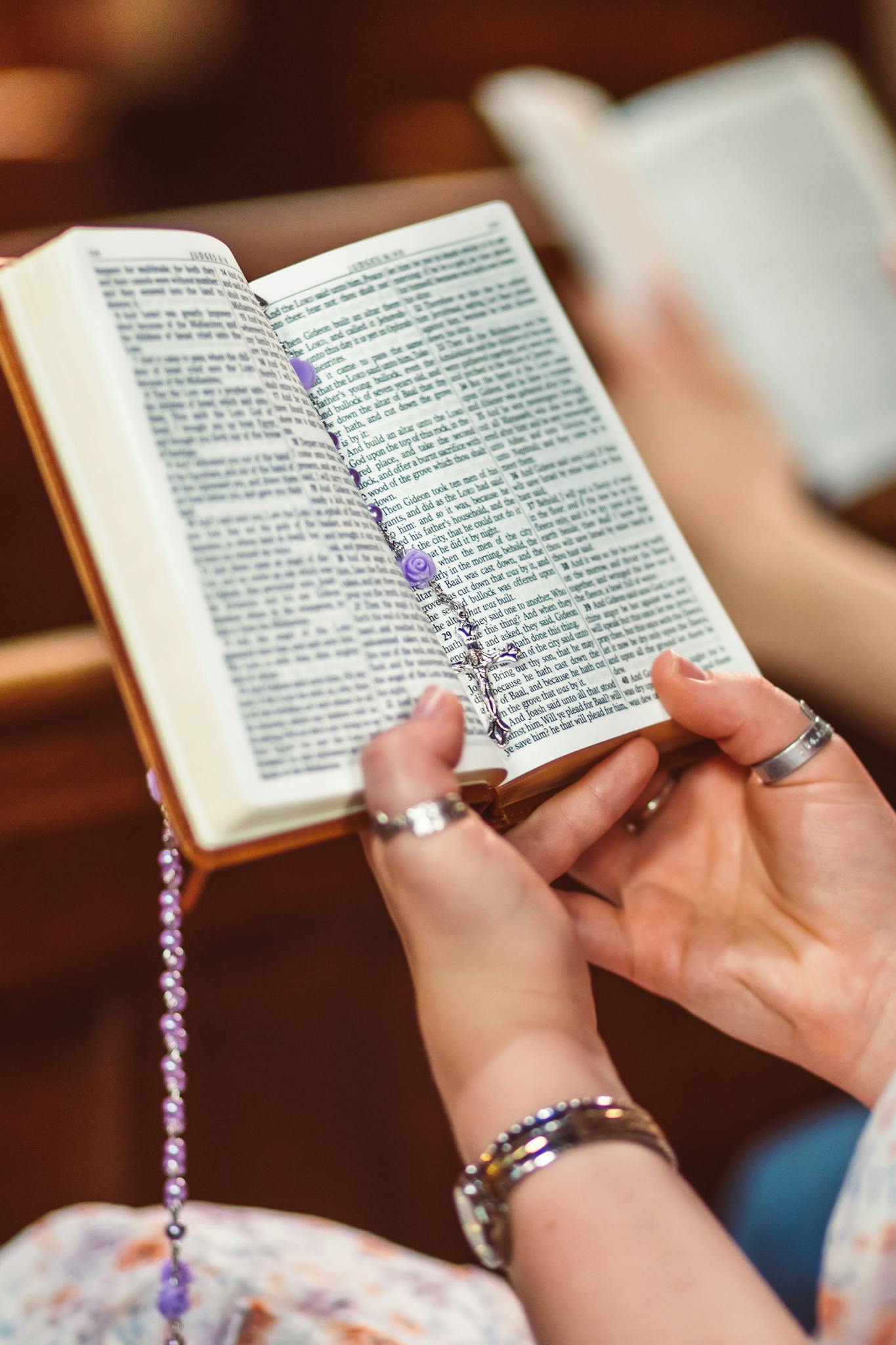 Adult holding an open Bible with delicate rosary beads, symbolizing faith and devotion.