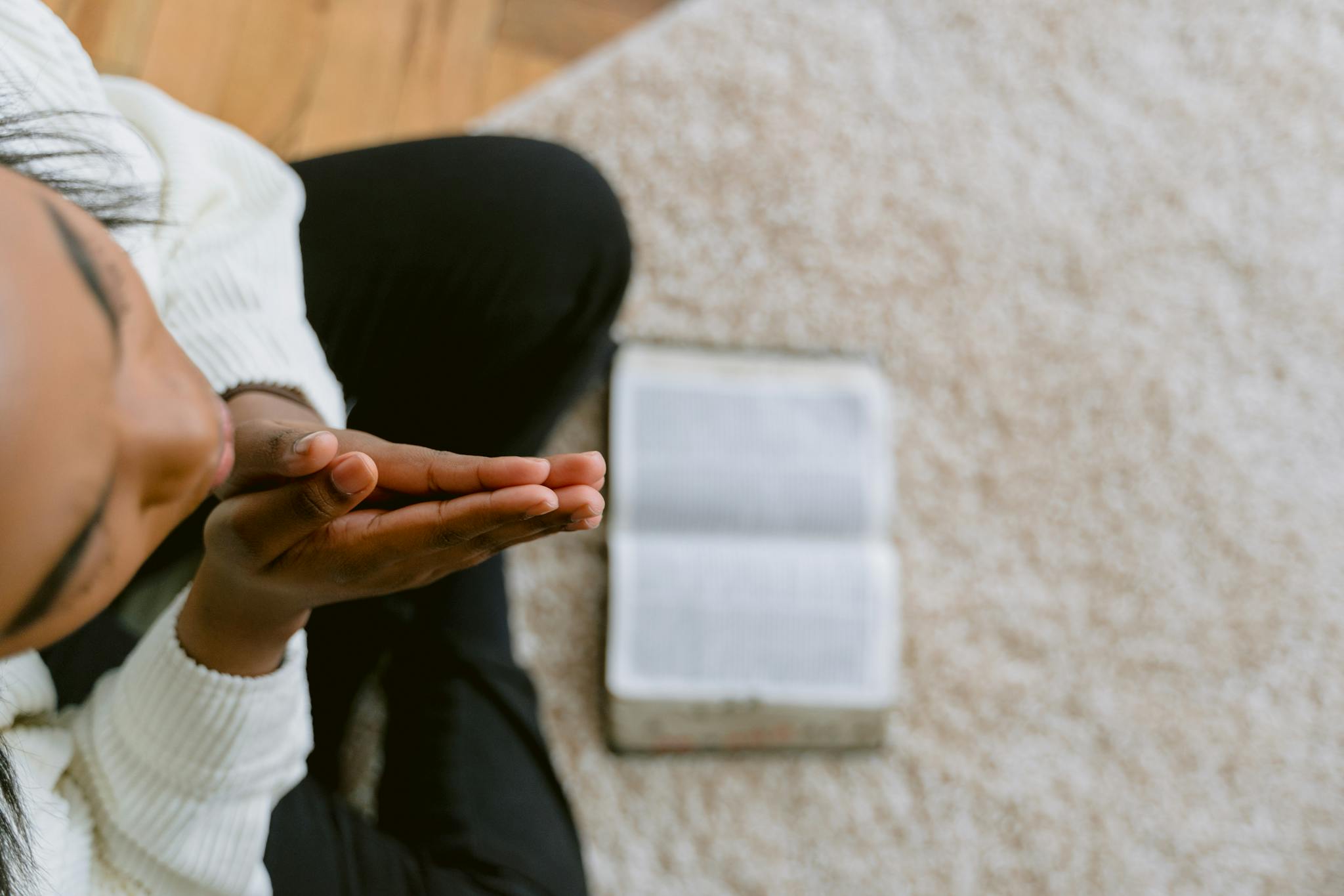 High angle view of a woman in prayer with an open Bible, symbolizing devotion and faith.