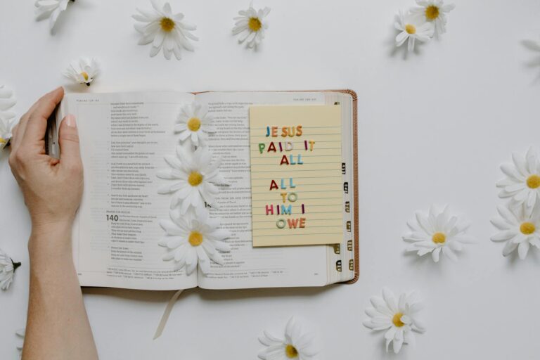 Open Bible with daisies and a note saying 'Jesus paid it all' creating a peaceful setting.